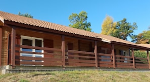 A wooden cabin with a tiled roof, wooden railings, and a grassy foreground.