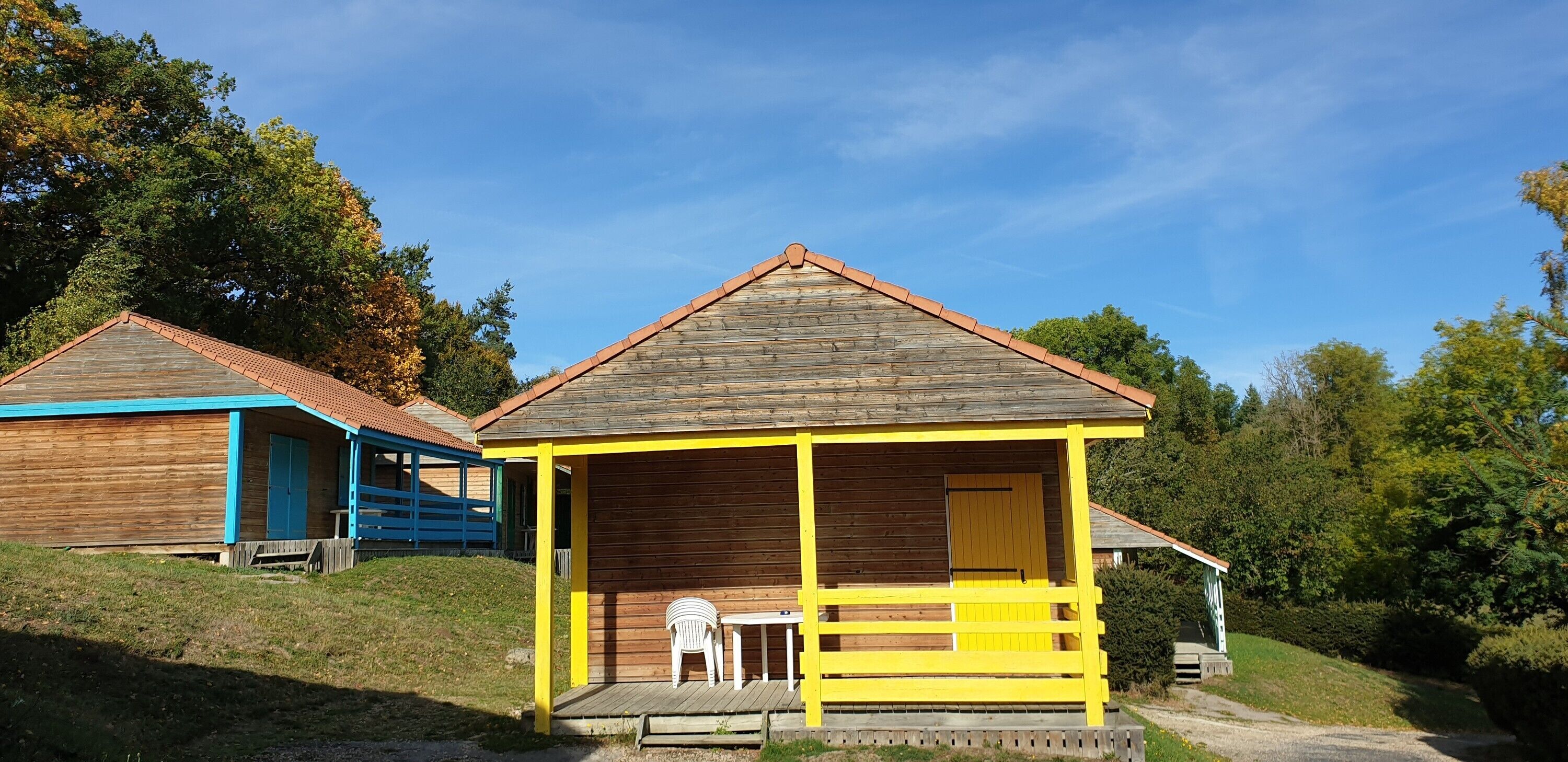 Two wooden cabins with a porch and a table, surrounded by trees.