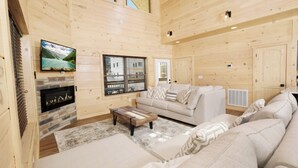 Un accogliente interno di una baita in legno, con un caminetto, un divano e una televisione fissata al muro.