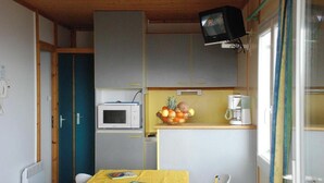 Cocina compacta con microondas, cafetera pequeña y frutero sobre la encimera.