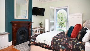 Ein Schlafzimmer mit Kamin, einem Bett mit floralem Bettzeug, einem Fernseher und Blick durch ein Fenster.