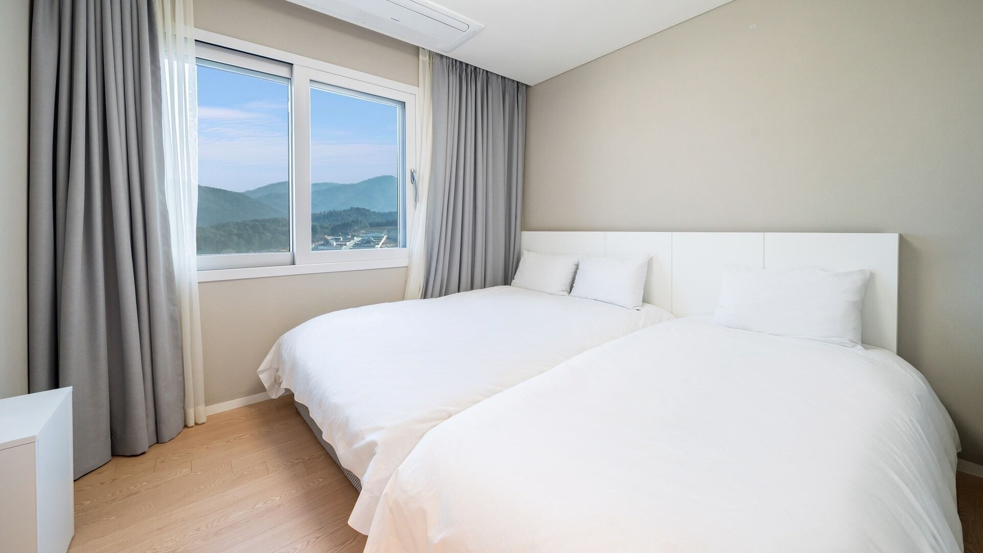 A hotel room with two beds, a large window with curtains, and a view of the mountains.