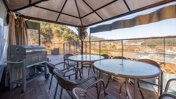 Un patio exterior con una parrilla, muebles de mimbre y vistas a un río y colinas.