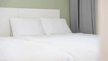 A bed with white bedding and pillows, a white headboard, and a grey curtain.