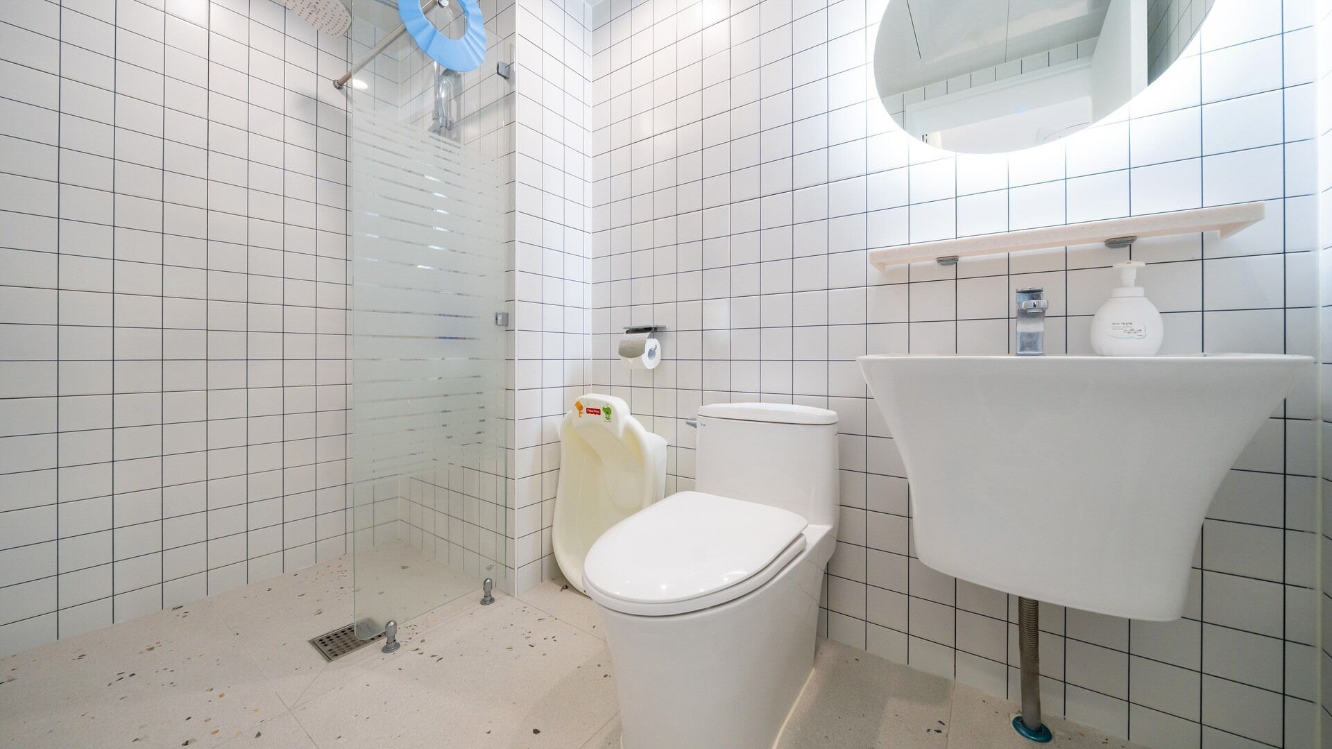 A bathroom with white tiled walls, a glass shower enclosure, a white toilet, and a sink with a mirror above it.