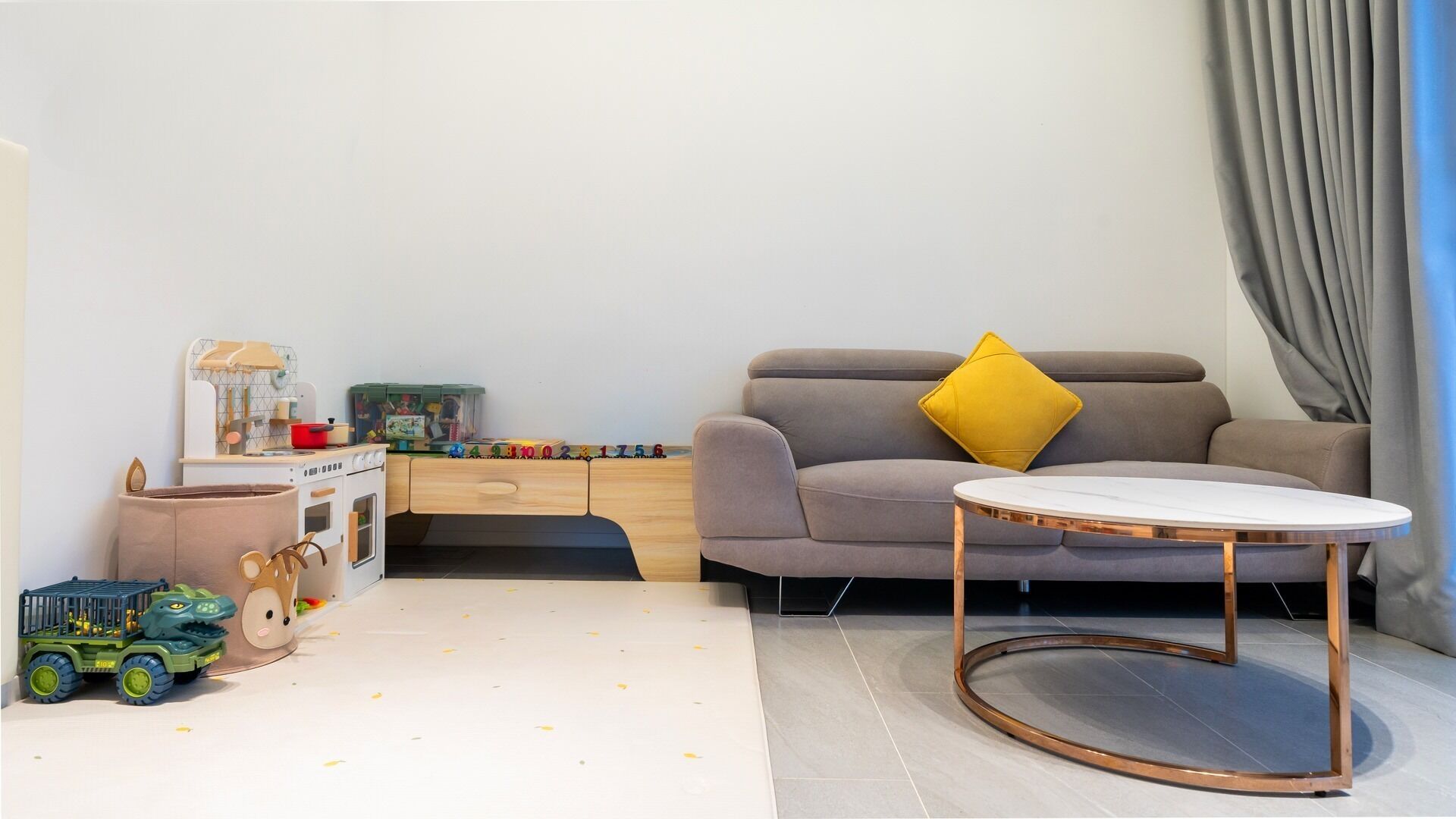 A modern living room with a sofa, a coffee table, a toy car, and a play area with toys and a toy stove.