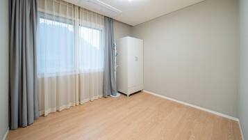 A room with a large window, grey curtains, a white wardrobe, and wooden flooring.