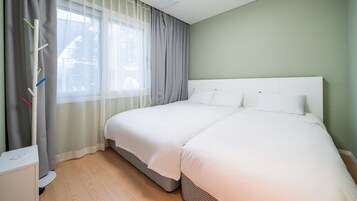 A hotel room with a large bed, a bedside table, a window with curtains, and a view of trees outside.