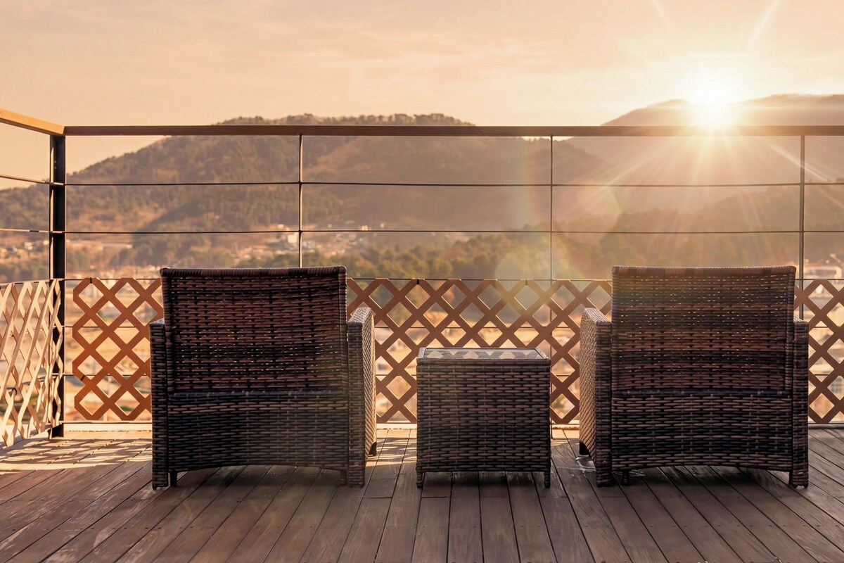 Eine Holzterrasse mit Korbmöbeln und Blick auf eine hügelige Landschaft.
