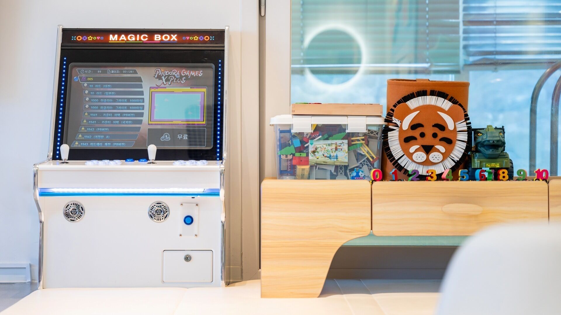 A children's play area with a 'MAGIC BOX' game machine and a wooden play table with alphabet blocks.