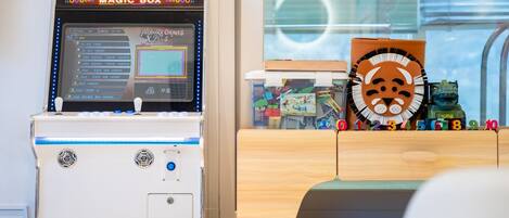 A children's play area with a 'MAGIC BOX' game machine and a wooden play table with alphabet blocks.