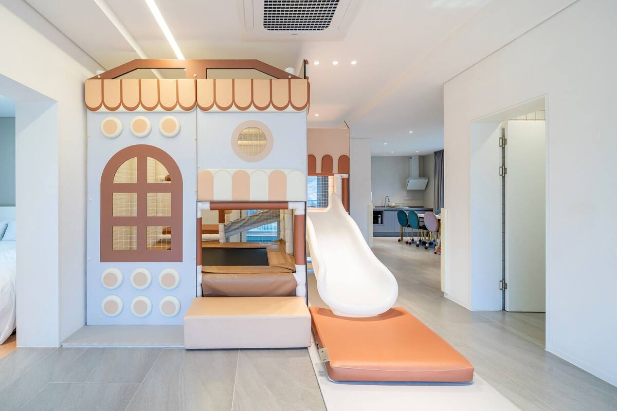 Un espace de jeux pour enfants avec un toboggan, des sièges rembourrés et une maison de jeux.