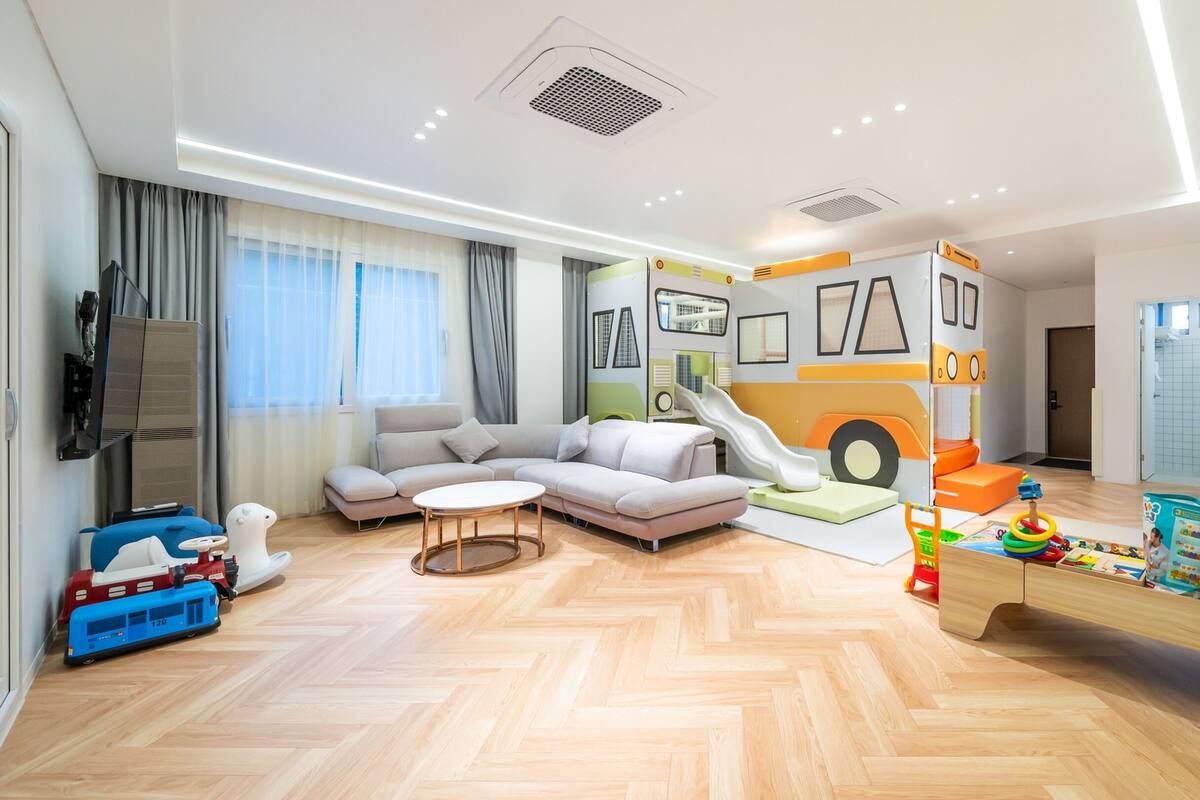Un salon moderne comprenant un canapé, une table basse, un espace de jeux avec un toboggan et un téléviseur fixé au mur.
