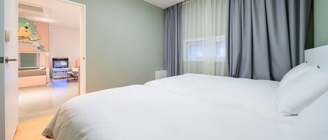 A hotel room with a large bed, a desk with a computer, and a bathroom visible through an open door.