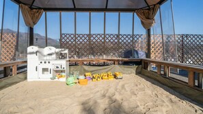 Eine Strandterrasse mit einer kleinen Küchenzeile, Spielzeug und einem Sandboden.