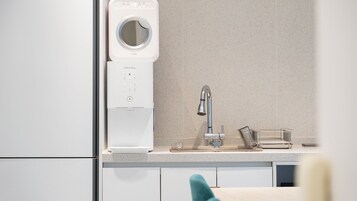 A modern kitchen with a built-in washing machine, a stainless steel faucet, and a small metal container on the countertop.