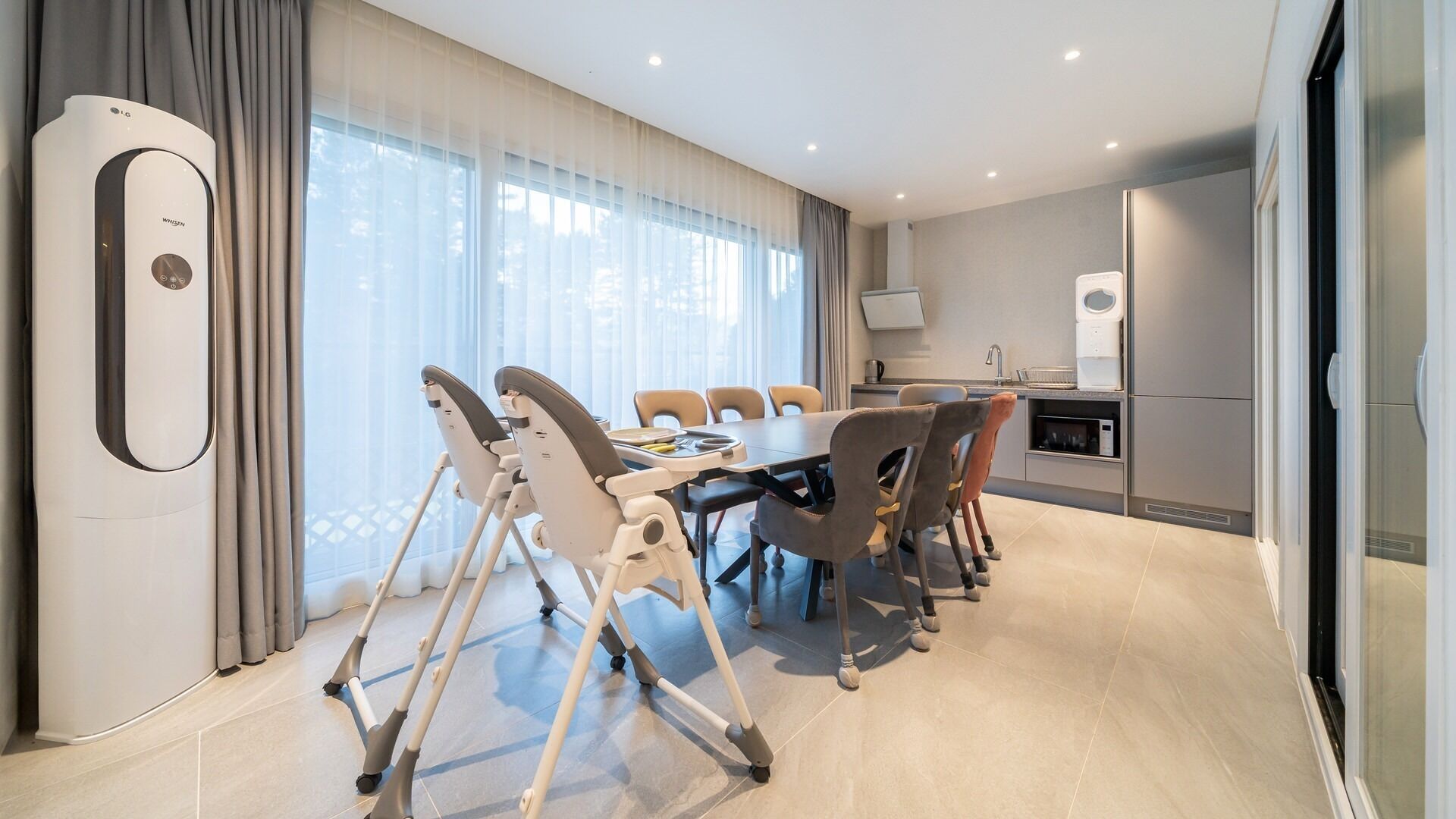 A modern hotel room with a dining area, a kitchenette, and a large window with curtains.
