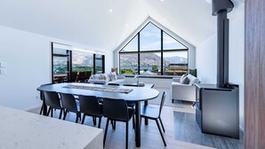 A modern living room with a large dining table, a fireplace, and large windows offering a mountain view.