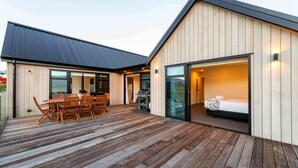A modern building with a wooden exterior, a covered patio with a table and chairs, and a bedroom with a bed and a nightstand.