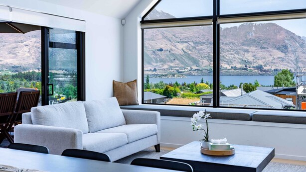 A modern living room with a large window offering a view of a lake and mountains.