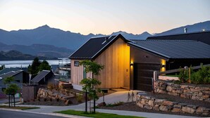 A modern house with a wooden exterior, a stone retaining wall, and a view of mountains.