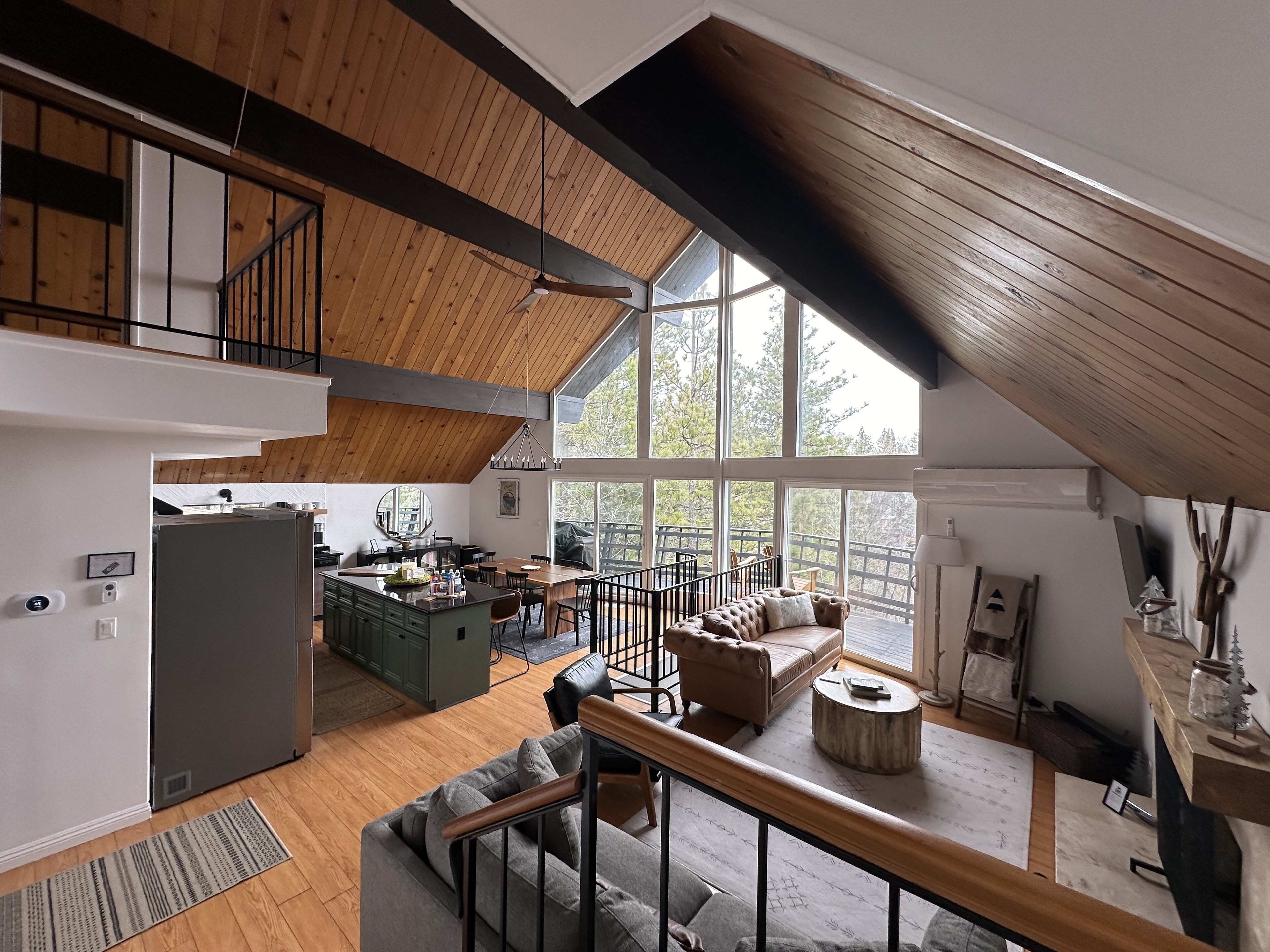 Un loft espacioso con techo alto, vigas de madera, zona de comedor, rincón de estar acogedor y grandes ventanales con vistas al exterior.