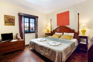Une chambre d’hôtel avec un lit, un téléviseur posé sur une commode, une fenêtre avec des rideaux et un tableau accroché au mur.