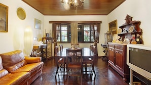 A dining room with a wooden table, chairs, a chandelier, and a television.
