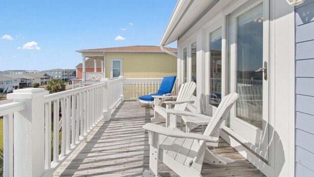 A wooden deck with white railings and two blue chairs.