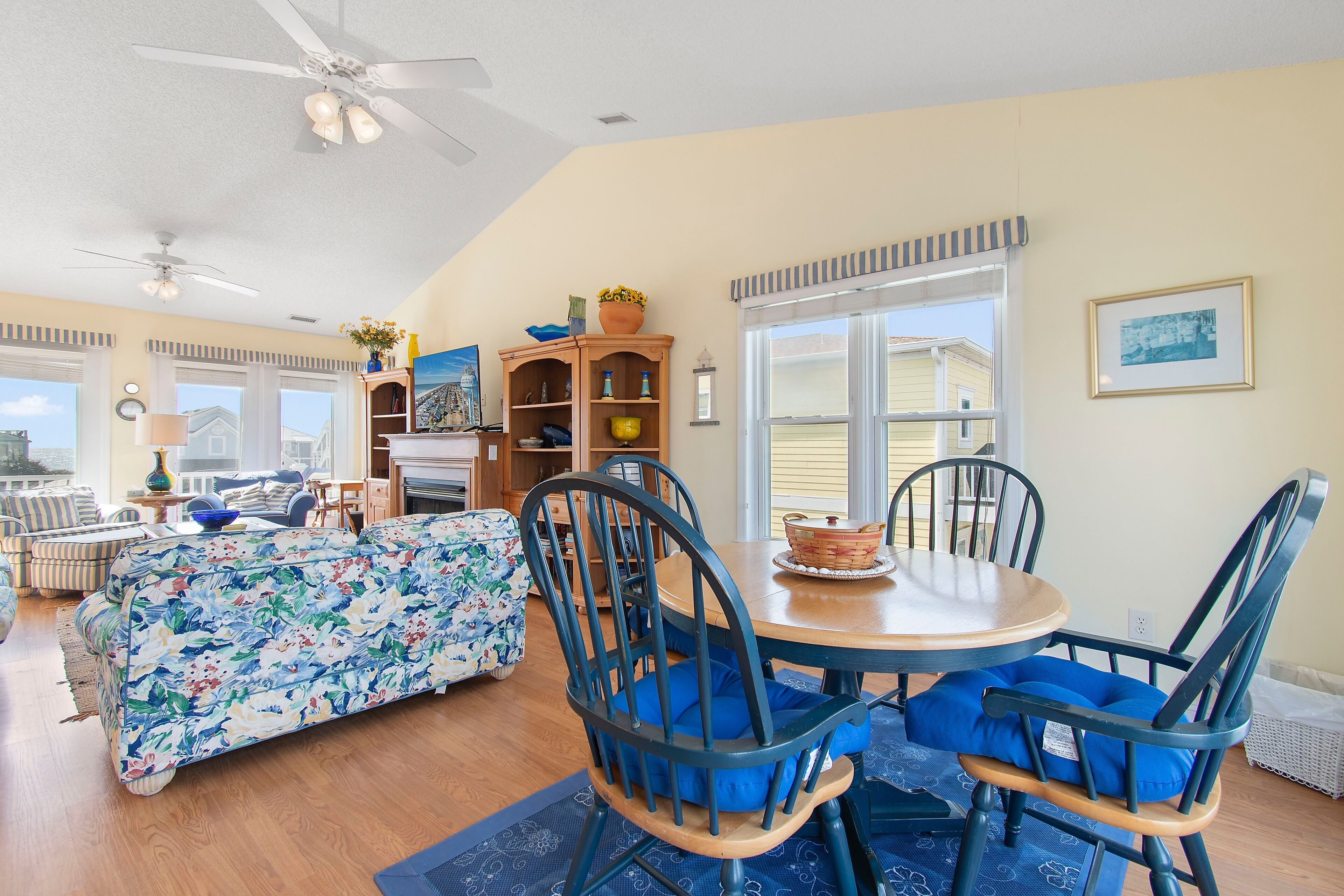 A dining area with a round table, blue cushioned chairs, and a floral sofa.