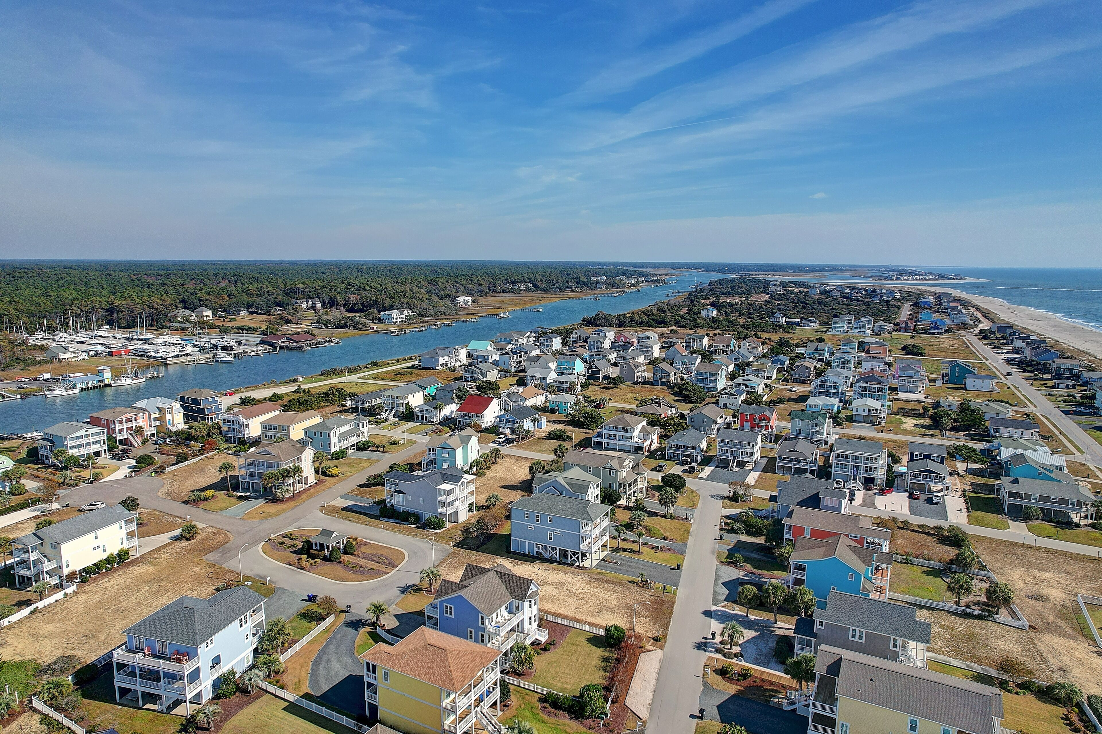 An aerial view of a coastal residential area with houses, a marina, and a beach.
