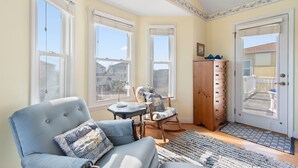 A room with a large window, a rocking chair, a wooden cabinet, and a door with a view to the outside.