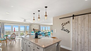 A spacious kitchen with a large island, wooden cabinets, and a view of the ocean through large windows.
