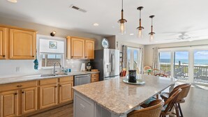 A kitchen with wooden cabinets, a granite countertop, and a view of the ocean through large windows.