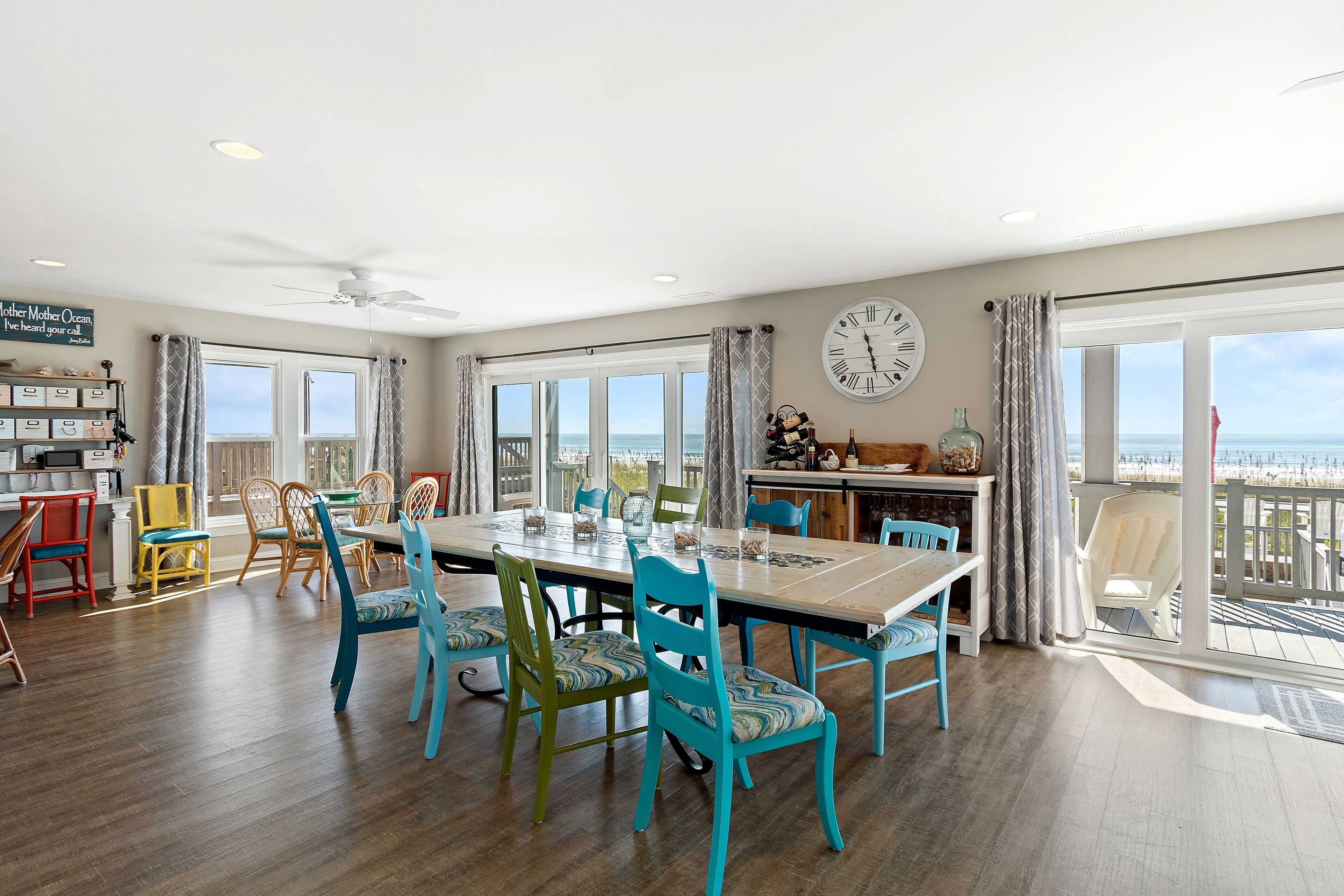 A spacious dining area with a large table and chairs, a kitchen area, and a view of the ocean.