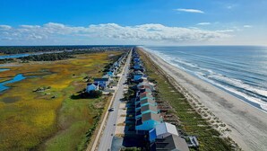 A coastal hotel with a long row of rooms facing the beach, a road running parallel to the beach, and a body of water to the left.