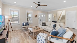 A living room with a TV, a ceiling fan, a coffee table, a sofa, and a staircase. - "Just Peachy" 3BR Home | 4 Baths (2 Full, 2 Half) (Oak Island)