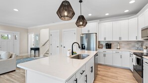 A modern kitchen with white cabinets, a central island, stainless steel appliances, and pendant lighting. - "Just Peachy" 3BR Home | 4 Baths (2 Full, 2 Half) (Oak Island)