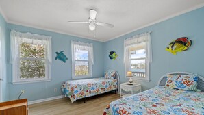Une chambre avec deux lits, un ventilateur de plafond et des décorations murales représentant des poissons.
