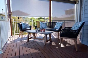 Een houten terras met een tafel en twee stoelen, een witte reling en uitzicht op de omgeving.