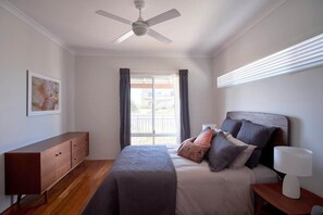 A bedroom with a bed, a nightstand, a ceiling fan, a window with curtains, and a wall-mounted light.