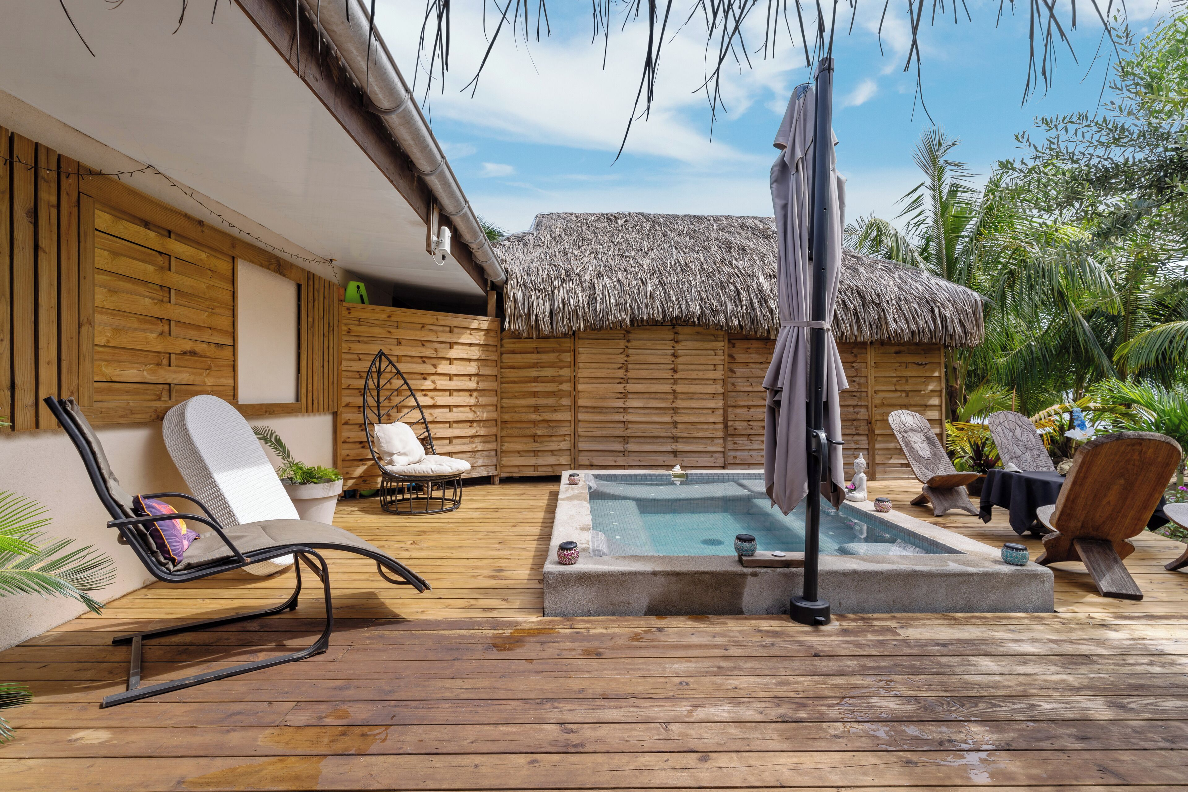A wooden deck with a hot tub, lounge chairs, and a thatched-roof structure.