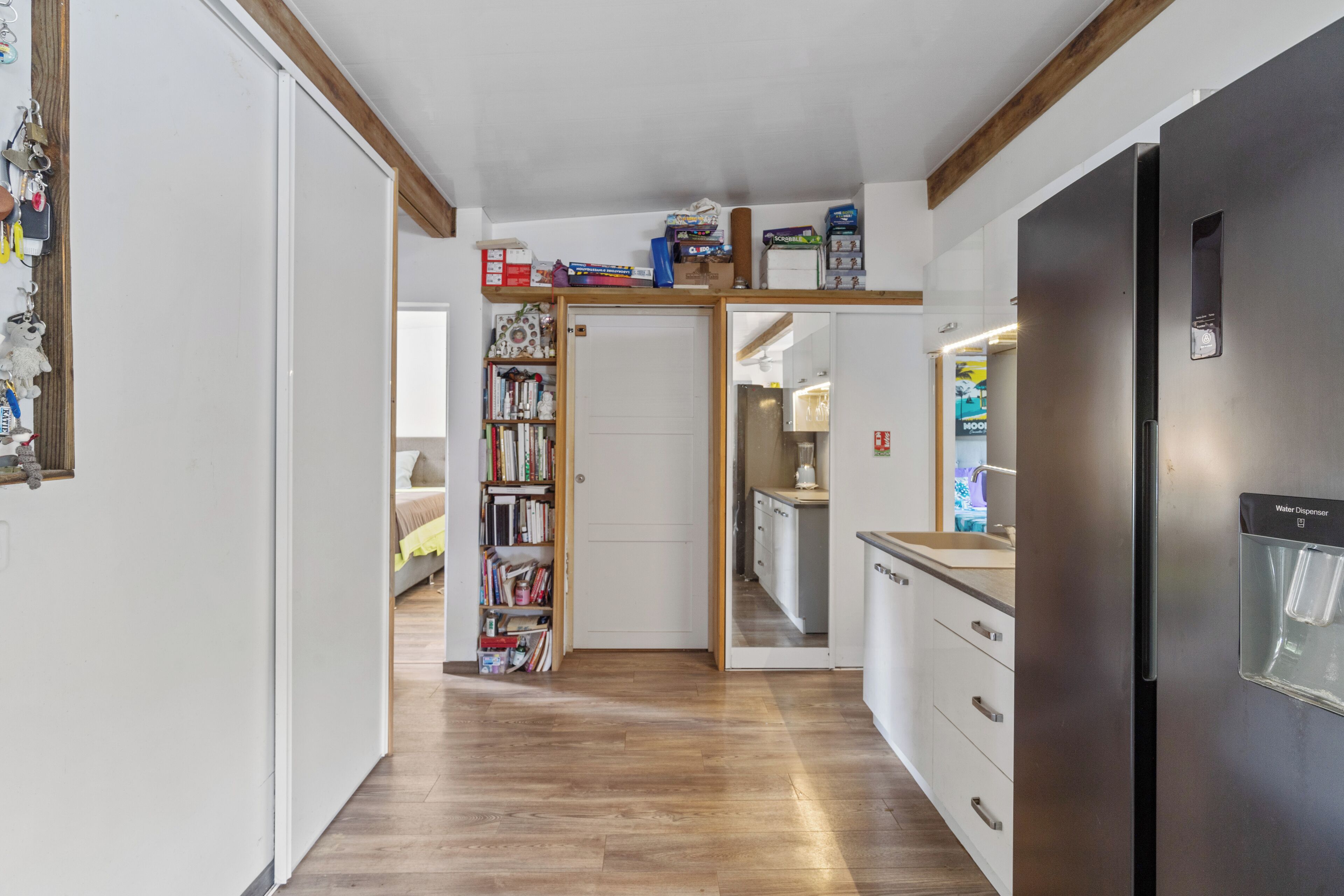 Una cocina moderna con refrigerador de acero inoxidable, piso de madera y una estantería empotrada.