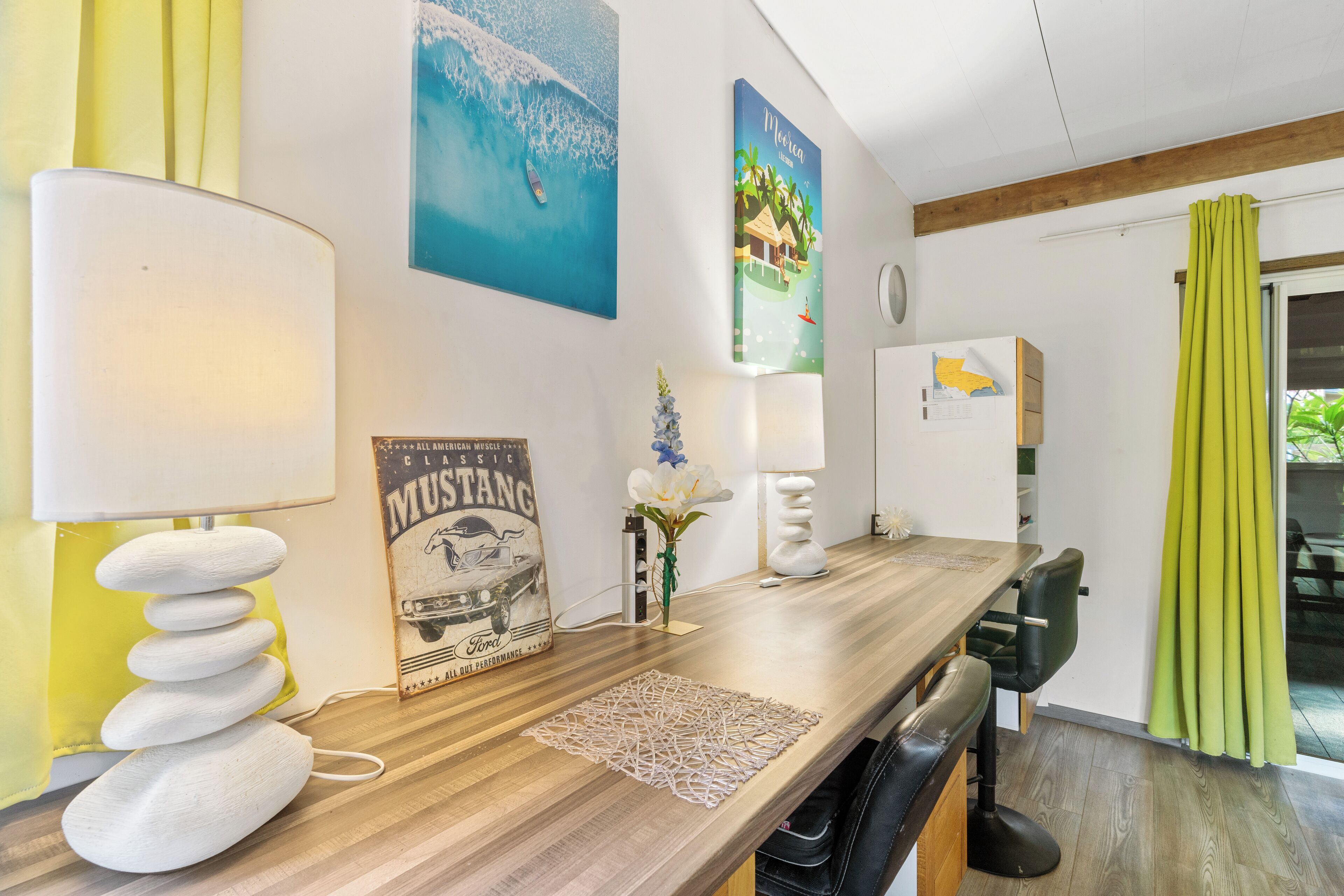 A modern kitchen with a wooden countertop, a stack of white stones, a vintage Ford Mustang poster, and a tropical-themed painting.