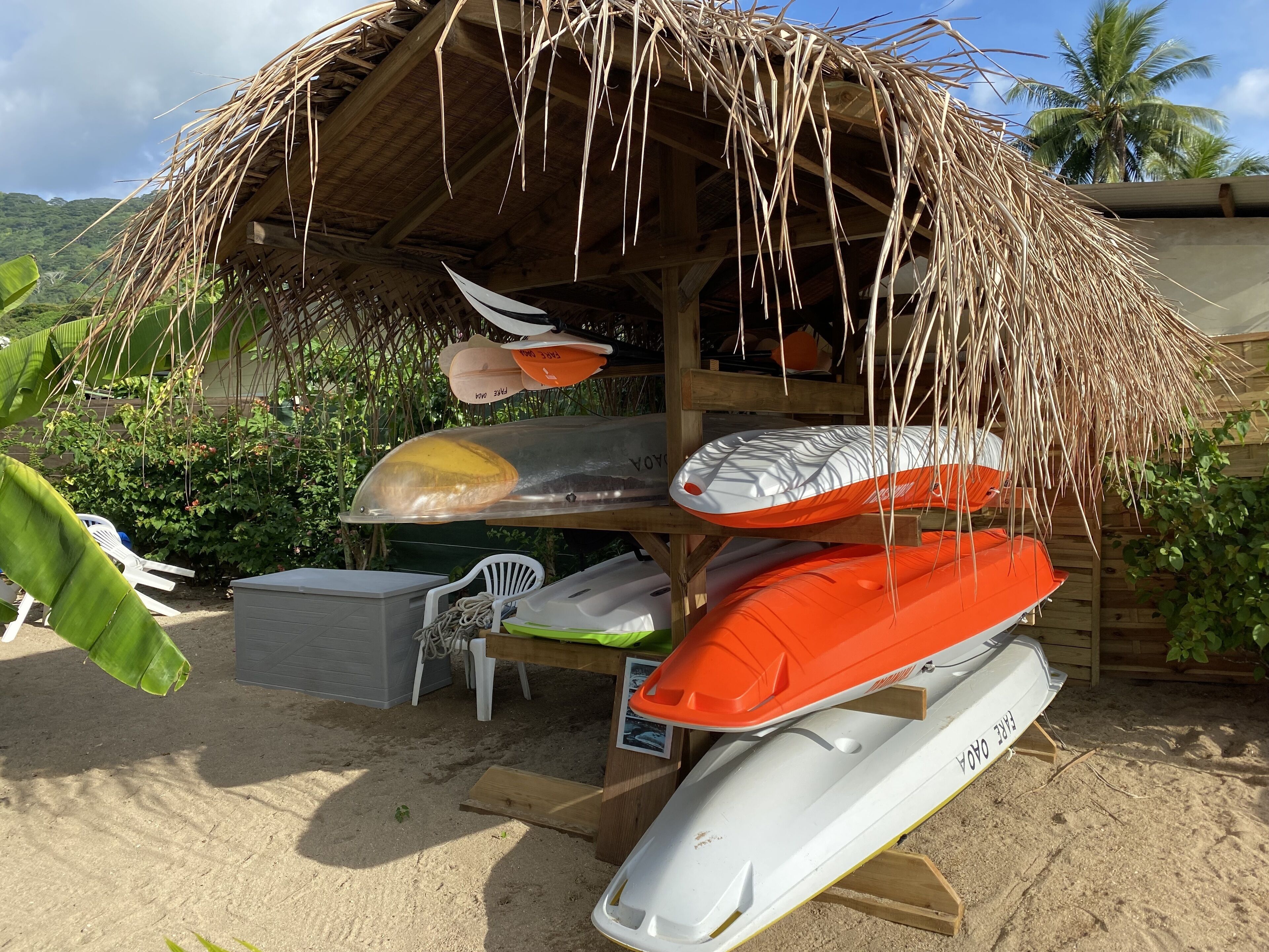 A thatched-roof structure with kayaks and a paddleboard stored underneath.