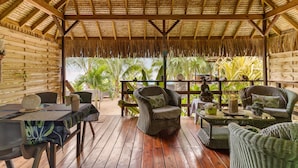 A covered outdoor seating area with wicker furniture, a table, and a view of palm trees. - Fare Oaoa Haapiti (Moorea-Maiao)