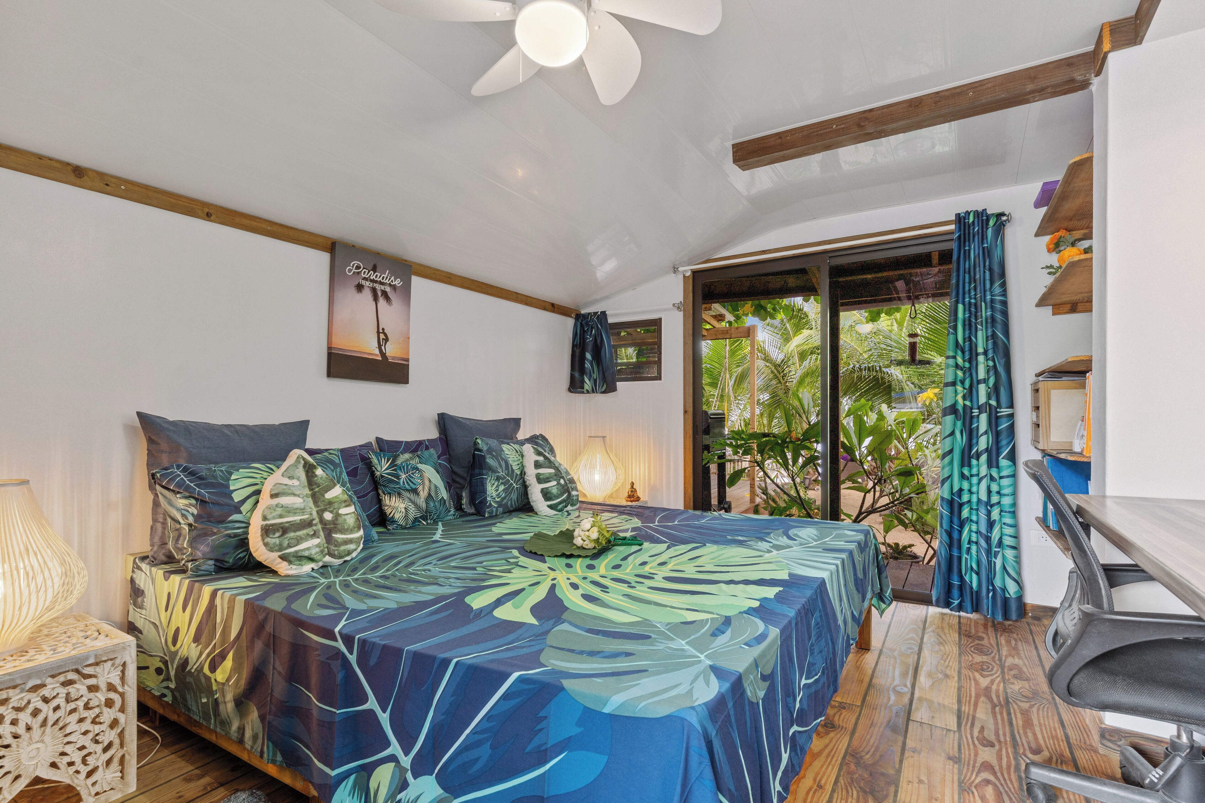 Een slaapkamer met een bed, bureau, stoel, plafondventilator en uitzicht op de omgeving.