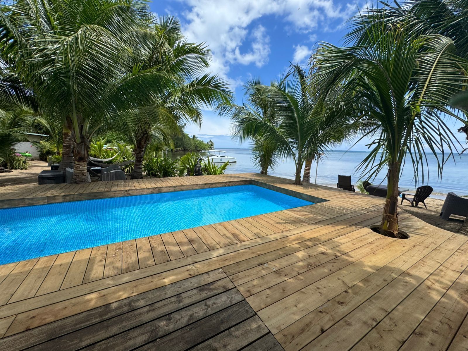 Una terraza de madera con piscina, rodeada de palmeras y vistas a un cuerpo de agua.