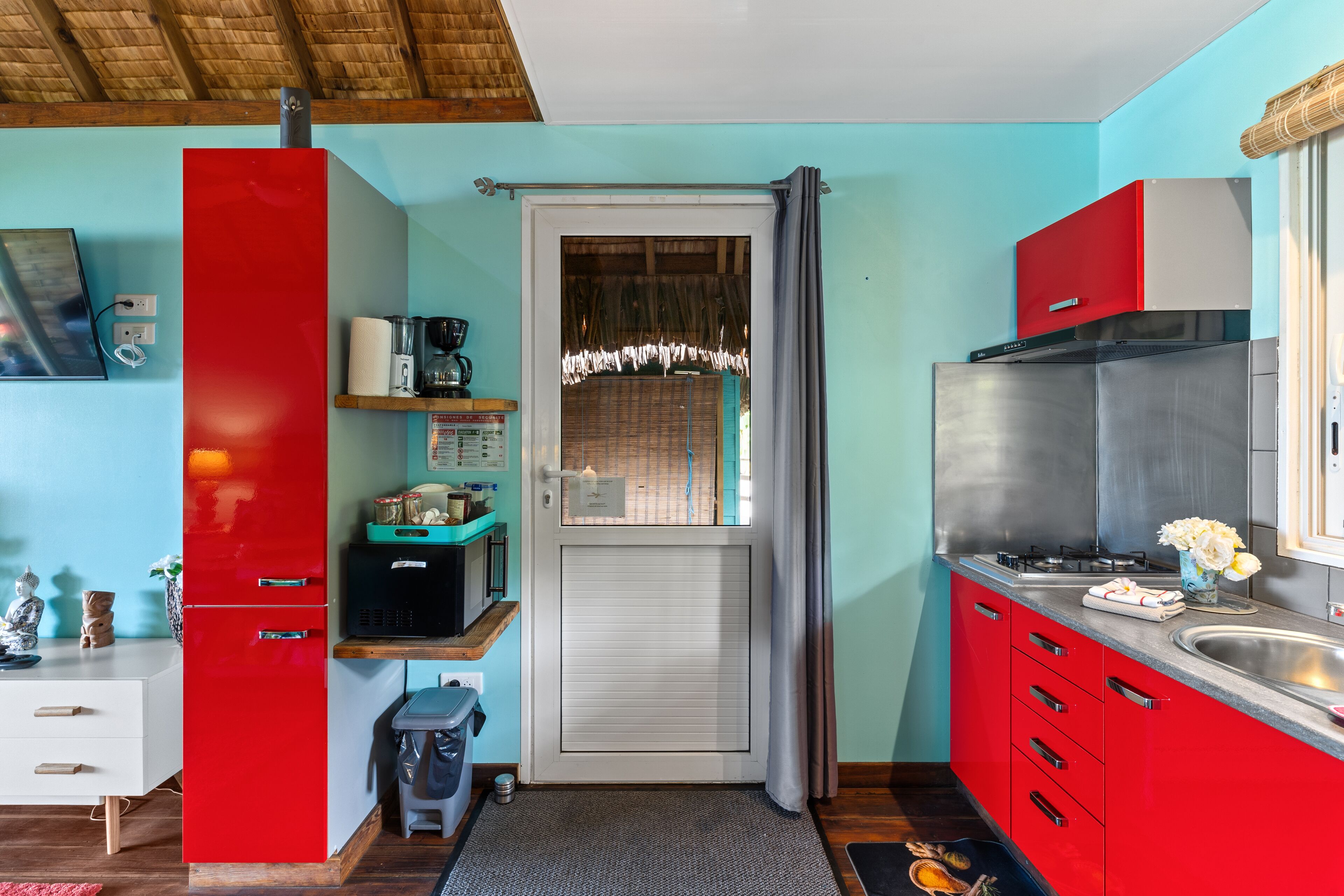 A compact kitchen with red cabinets, a stainless steel refrigerator, a coffee machine, and a sink.