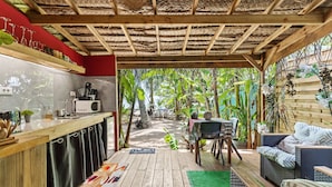 A covered outdoor area with a wooden deck, a kitchen area with a microwave and sink, and a seating area with a wicker sofa and chairs. - Fare Oaoa Haapiti (Moorea-Maiao)